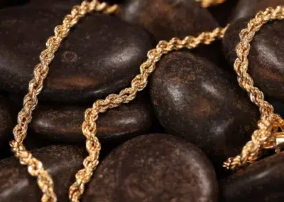 A 14 Karat Yellow Gold Figaro 25" Chain necklace draped over dark polished stones.