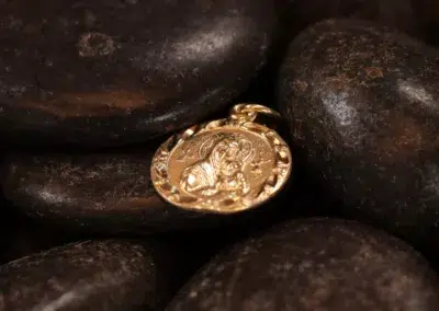 A 14 Karat Yellow Gold Figaro 25" Chain nestled among dark pebbles.