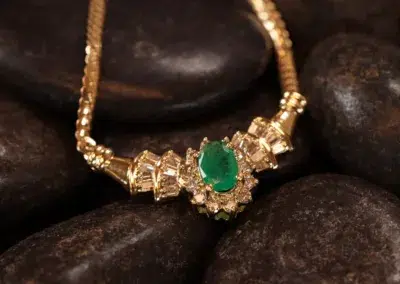 14 Karat Yellow Gold Figaro 25" Chain featuring a green gemstone pendant, displayed on a bed of smooth dark stones.