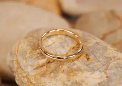 A 14 Karat Yellow Gold Comfort Fit Band Size 7 wedding ring sitting on a rock.