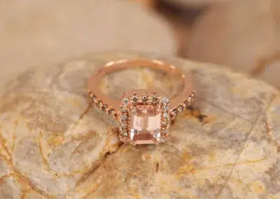 An engagement ring with a morganite stone on top of rocks features a 14 Karat Yellow Gold Comfort Fit Band.
