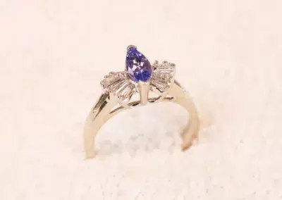 A tanzanite and diamond ring with a 14 Karat Yellow Gold Comfort Fit Band sitting on top of snow.