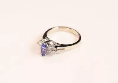A tanzanite and diamond ring on a white surface, featuring the 14 Karat Yellow Gold Comfort Fit Band.