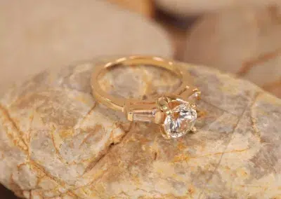 A 14 Karat Yellow Gold Comfort Fit Band with a baguette cut diamond on top of rocks.