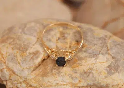 A 14 Karat Yellow Gold Comfort Fit Band with a black stone on top of rocks.
