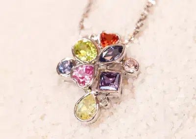 A necklace with multi-colored stones on top of sand, featuring a 14 Karat Yellow Gold Comfort Fit Band.