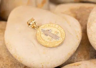 14K YG Pendant with an airplane motif and a tanzanite accent resting on a smooth pebble.