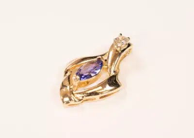 14K YG Tanzanite & Diamond Pendant in the shape of a swan, featuring a tanzanite gemstone and a small clear crystal, against a white background.