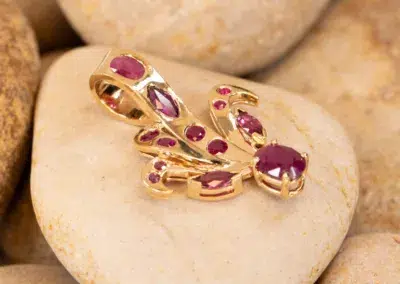 A 14K YG Tanzanite & Diamond Pendant with pink tanzanite gemstones resting on smooth, beige stones.