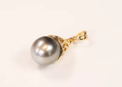 A single pearl earring with a gold setting and a 14K YG Tanzanite & Diamond pendant on a white background.
