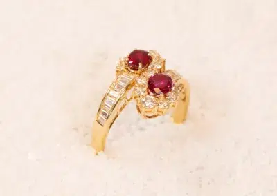 14K YG Tanzanite & Diamond Pendant with two red gemstones and surrounding diamonds, displayed on a white sandy texture.