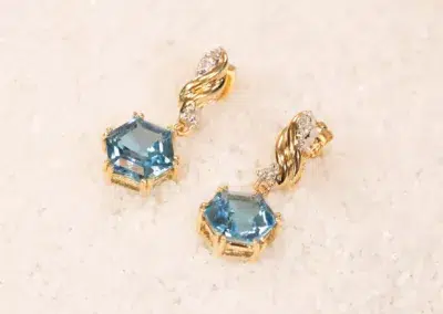 A 14K YG Tanzanite & Diamond Pendant with tanzanite gemstones and diamond accents on a sandy textured background.
