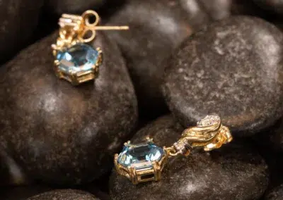 A 14K YG Tanzanite & Diamond pendant with blue gemstones resting on dark pebbles.