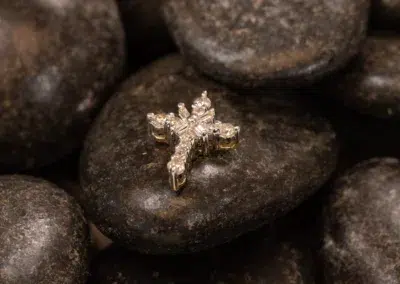 A 14K YG Tanzanite & Diamond pendant resting on dark, smooth pebbles.