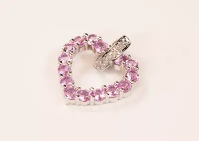 Silver ring with embedded diamonds resting on a circular pink crystal bracelet, displayed against a plain beige background adorned with a 14K YG Tanzanite & Diamond Pendant.
