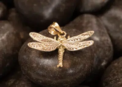 A 14K YG Tanzanite & Diamond pendant with a Tanzanite rests on smooth dark stones.