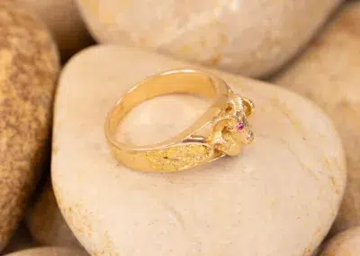 10 Karat Yellow Gold Ram Ring designed with small gemstones, displayed on a smooth, beige stone surface.