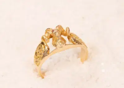 10 Karat Yellow Gold Ram Ring with intricate leaf design and small diamond accents displayed on a white grainy surface.