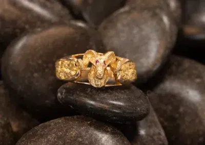 Golden 10 Karat Yellow Gold Ram Ring with red eyes and diamond features, crafted in 10 karat yellow gold, displayed on dark smooth pebbles.