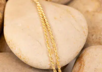 A 10 Karat Yellow Gold Ram Ring draped over a smooth, beige pebble.
