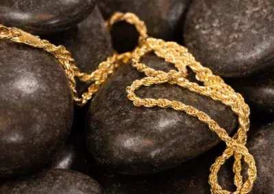 A 10 Karat Yellow Gold Ram Ring casually draped over smooth, dark pebbles.