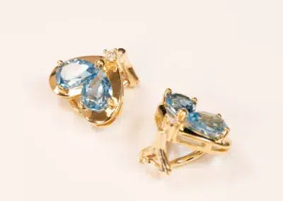 Pair of 10 karat yellow gold Ram Rings with oval light blue gemstones on a cream background.
