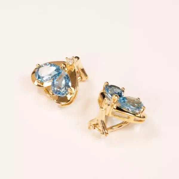Pair of 10 karat yellow gold Ram Rings with oval light blue gemstones on a cream background.
