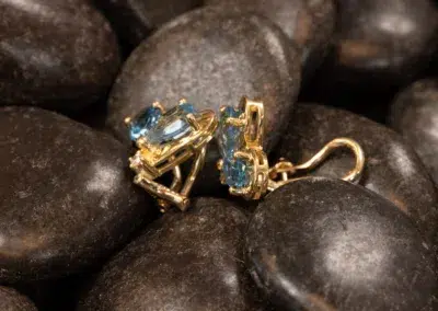 10 Karat Yellow Gold Ram Ring earrings with blue gemstones resting on dark polished stones.