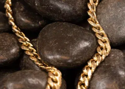 A close-up image of a gold chain resting on dark, smooth stones featuring the 10 Karat Yellow Gold Ram Ring.