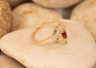 10 Karat Yellow Gold Ram Ring with a central ruby and diamond accents resting on a smooth, beige stone.
