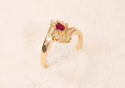 10 Karat Yellow Gold Ram ring with a central ruby and diamond accents, displayed on a white sandy surface.