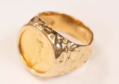 10 Karat Yellow Gold Ram ring with a textured band and embossed coin design on top, displayed against a plain white background.