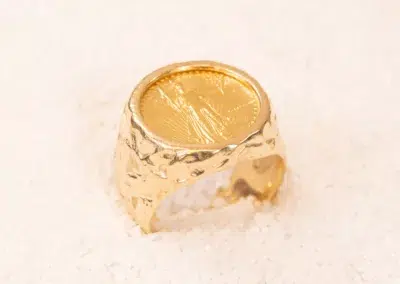 10 Karat Yellow Gold Ram Ring with engraved surface, positioned upright on a white sandy texture.