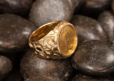 A 10 Karat Yellow Gold Ram Ring featuring an embossed coin design, nestled among dark, rounded stones.