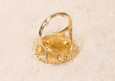 10 Karat Yellow Gold Ram Ring embedded with small clear stones, resting on a white sandy surface.