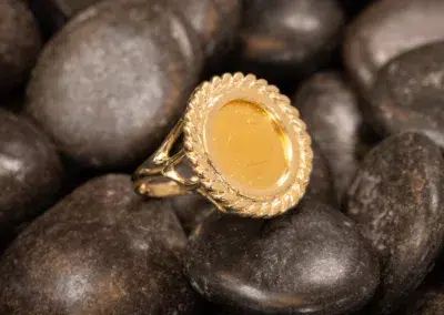 A 10 Karat Yellow Gold Ram Ring with an oval amber center set atop smooth, dark pebbles.
