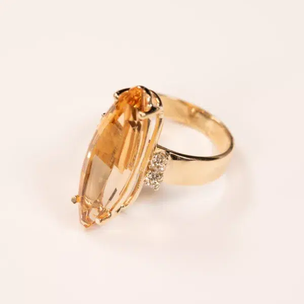 14K YG Diamonds & Peach Tourmaline Ring featuring a large, oval-shaped peach tourmaline gemstone flanked by small diamonds, set against a white background.