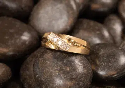 14K YG Diamonds & Peach Tourmaline Ring placed on dark, polished river stones.