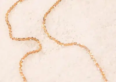 A delicate 14K YG Diamonds & Peach Tourmaline Ring gracefully arranged on a white sandy texture.