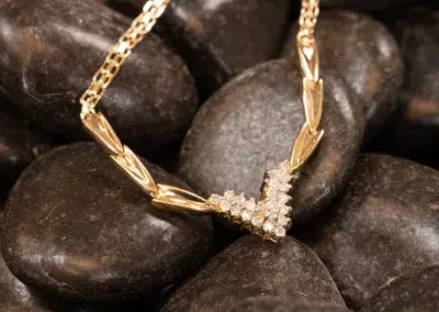 14K YG Diamonds & Peach Tourmaline Ring with a diamond pendant resting on smooth, dark stones.