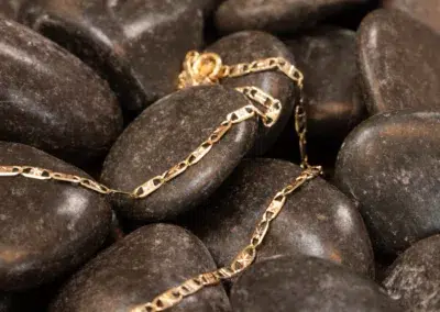 A 14K YG Diamonds & Peach Tourmaline Ring draped over smooth, dark pebbles.