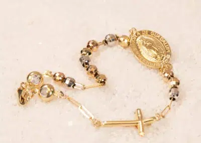Gold and silver-toned bead bracelet with a circular 14K YG Diamonds & Peach Tourmaline Ring featuring religious imagery, displayed on a light, textured surface.