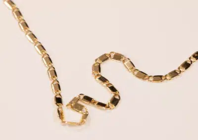 Gold chain with interlocking links on a plain beige background, featuring a 14K YG Diamonds & Peach Tourmaline Ring clasp.