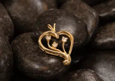 A 14K YG Diamonds & Peach Tourmaline ring with small peach tourmaline gems, resting on a background of smooth, dark stones.
