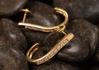 Gold hoop earrings set with diamonds resting on smooth black stones, crafted in 14K YG.