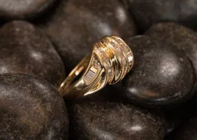14K YG Diamonds & Peach Tourmaline Ring with intricate details and diamonds, resting on dark, smooth stones.
